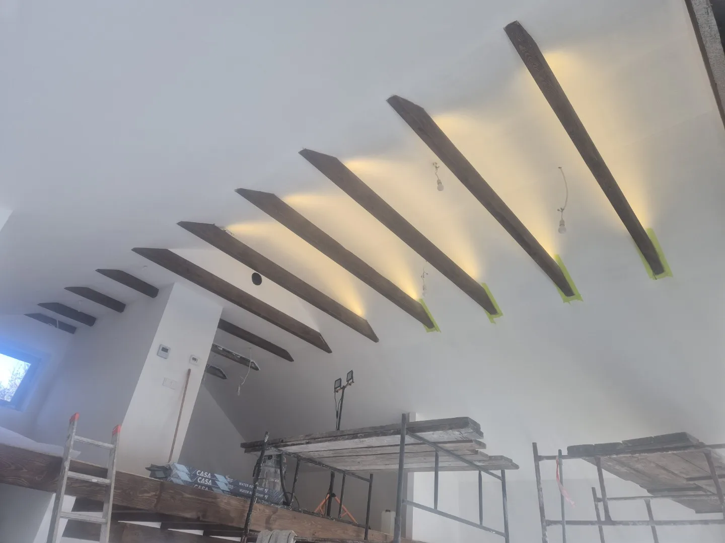 Zdjęcie przedstawia nowoczesny sufit dachowy z ciemnymi belami w zabudowie, gdzie zastosowano efekt „spadane światło" dl