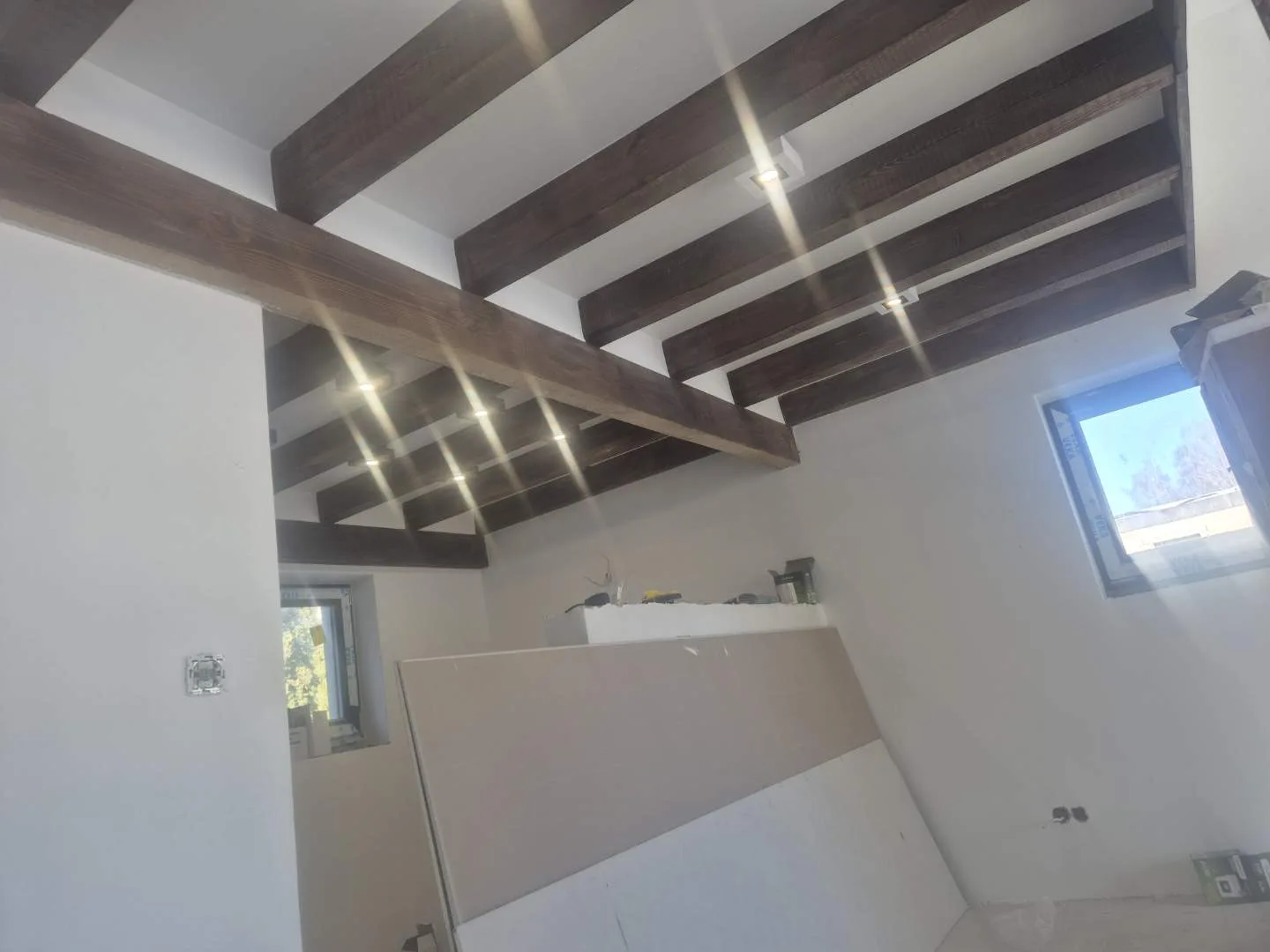 Nowoczesne wnętrze w trakcie prac remontowych, charakteryzujące się ciemnymi belkami stropowymi ozdobionymi wkomponowany